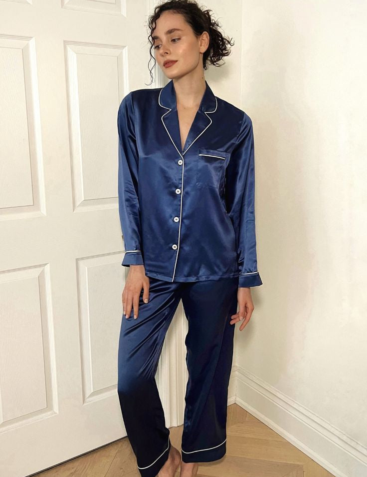 Woman wearing a blue satin pajama set in a room with white walls and wooden flooring.